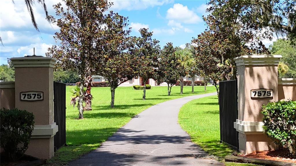 A paved driveway leads through a gated entrance toward a house surrounded by green lawns — 7571 W HIGHWAY 326, OCALA, FL
