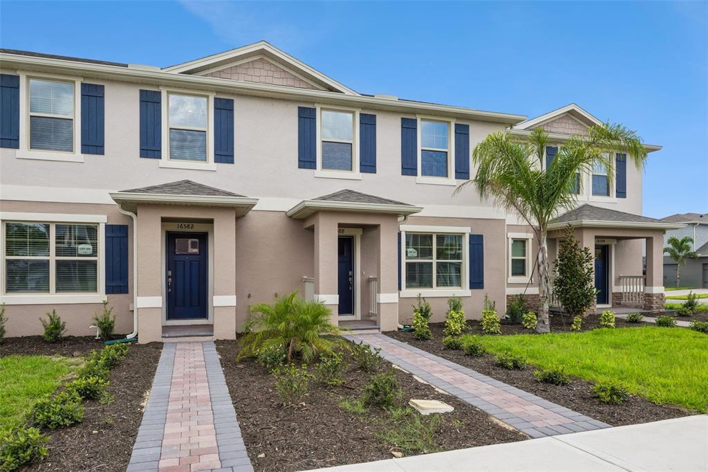 A row of two-story townhomes with beige stucco siding, blue shutters, and paved walkways — 16588 BARBOURS CREEK WAY, WINTER GARDEN, FL