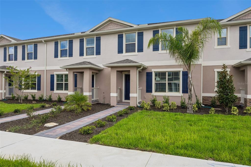 A two-story townhouse exterior features beige stucco walls, blue shutters, and a small front lawn — 16588 BARBOURS CREEK WAY, WINTER GARDEN, FL