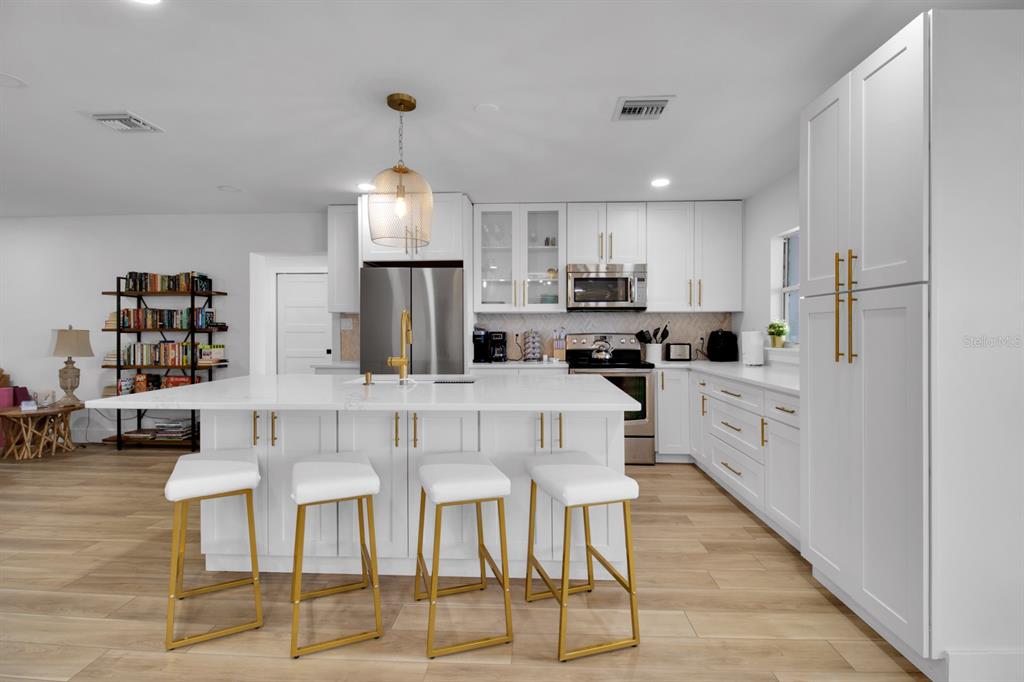 A modern kitchen features white cabinetry, a large central island with bar seating, and wood-look flooring — 1155 LEMON BLUFF ROAD, OSTEEN, FL