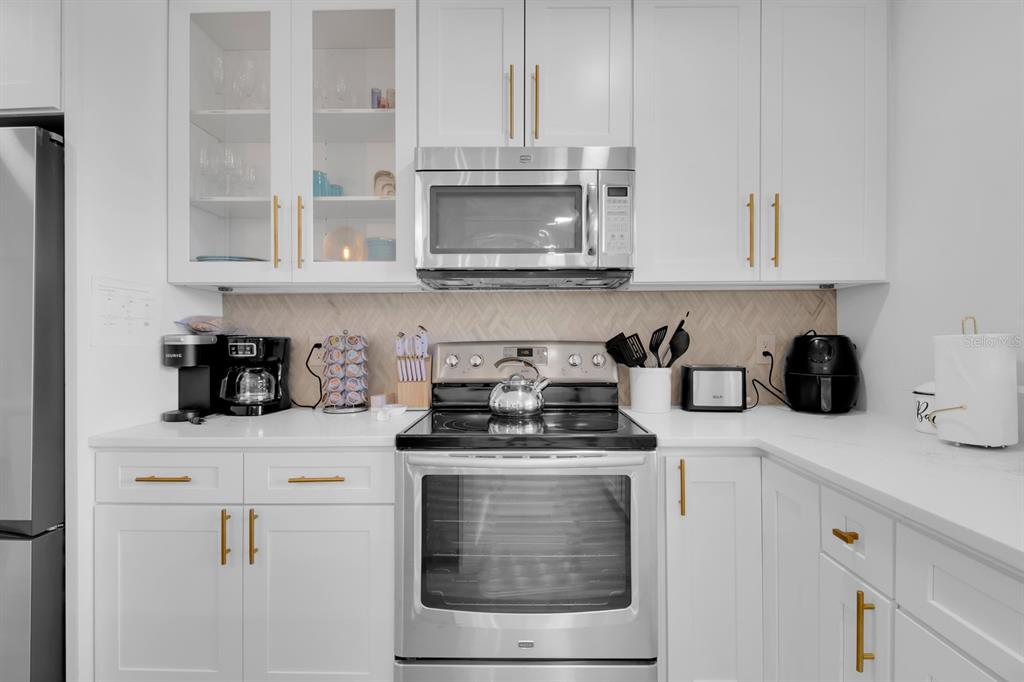 A kitchen features white cabinets, stainless steel appliances, and a light-colored herringbone tile backsplash — 1155 LEMON BLUFF ROAD, OSTEEN, FL