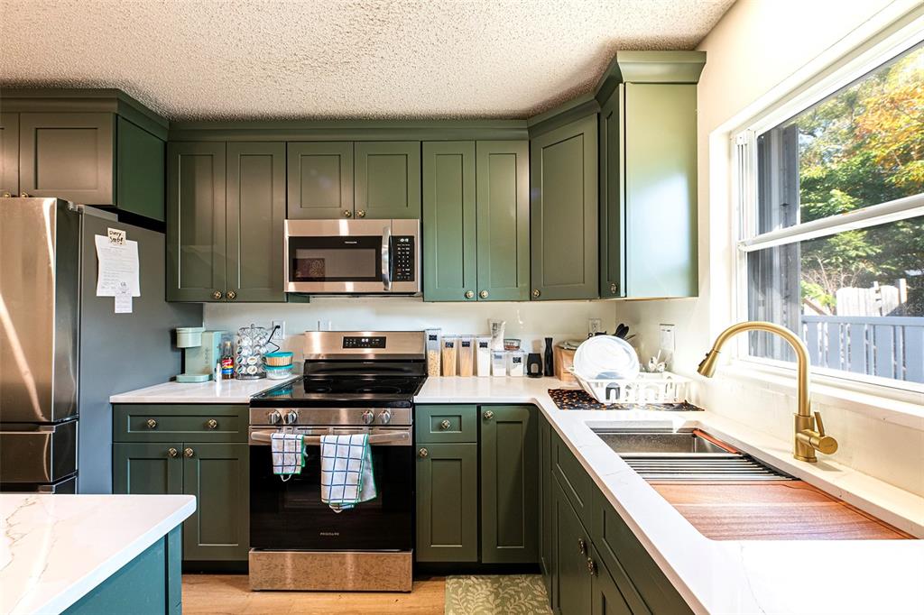 A kitchen features green cabinets, stainless steel appliances, white countertops, and a gold faucet — 6401 CEDARBROOK DRIVE S, PINELLAS PARK, FL