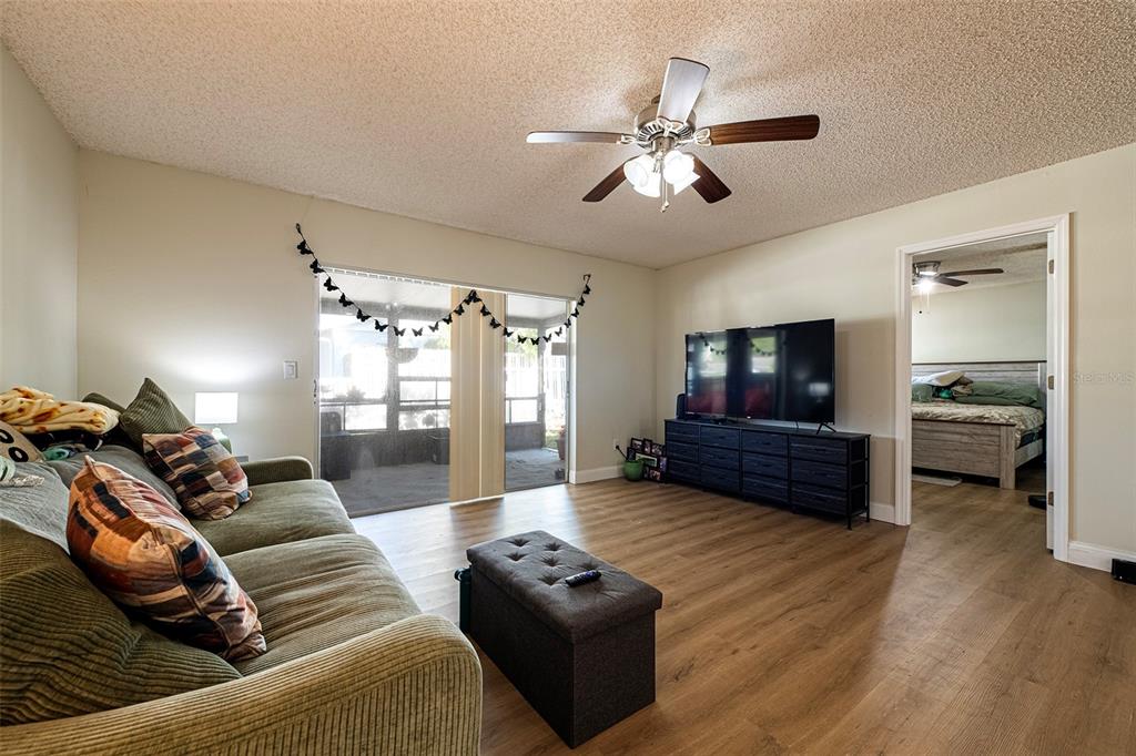 A living room features wood-look flooring, a ceiling fan, a sofa, and a television console — 6401 CEDARBROOK DRIVE S, PINELLAS PARK, FL