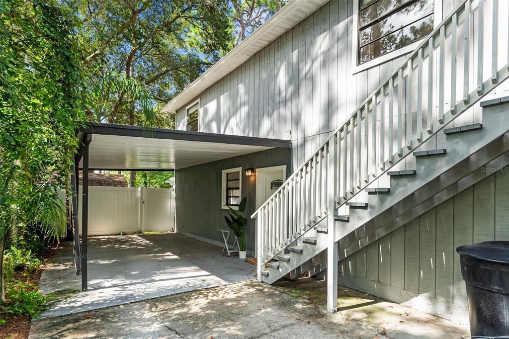 A white front door with a welcome mat sits beside an outdoor staircase under a carport — 138 69TH AVENUE N, ST PETERSBURG, FL