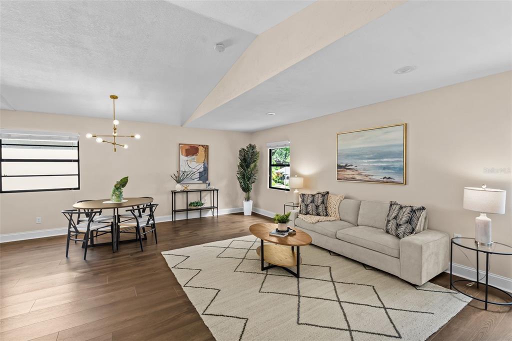 An open-concept living and dining area features wood-look flooring, a vaulted ceiling, and neutral walls — 138 69TH AVENUE N, ST PETERSBURG, FL