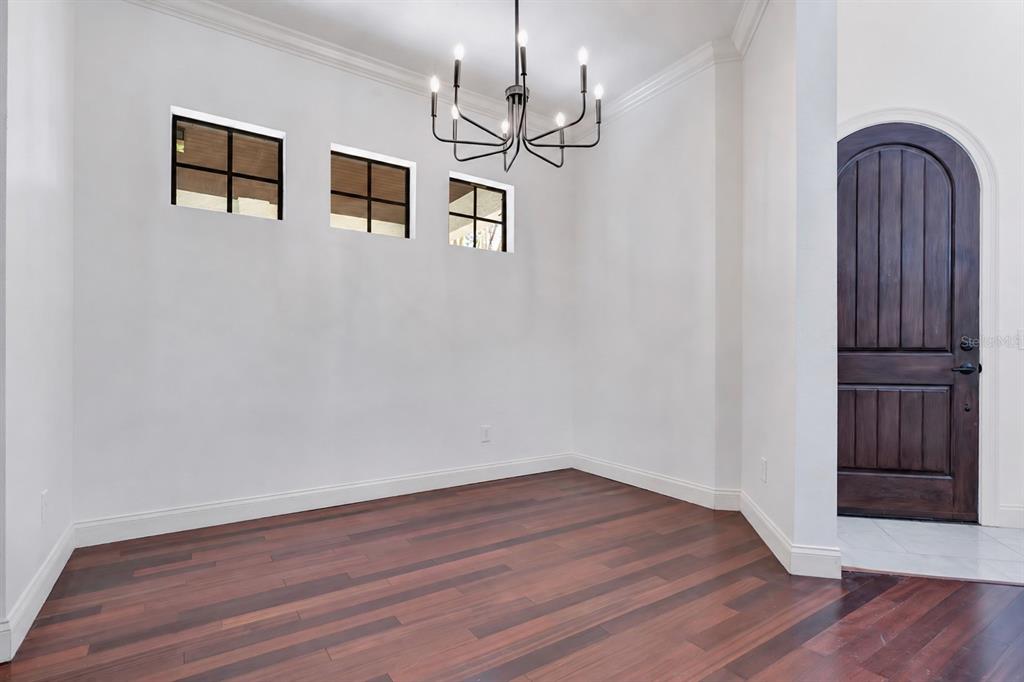A dining room with dark wood flooring, a chandelier, three small windows, and an arched door — 134 E ESTHER STREET UNIT A, ORLANDO, FL