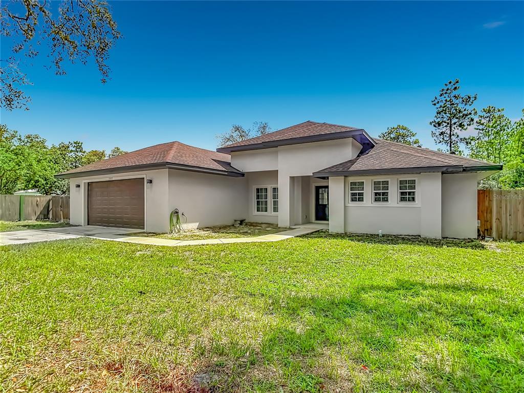 A single-story house with a brown garage door, light-colored stucco walls, and a shingled roof — 15032 HUMMINGBIRD ROAD, WEEKI WACHEE, FL