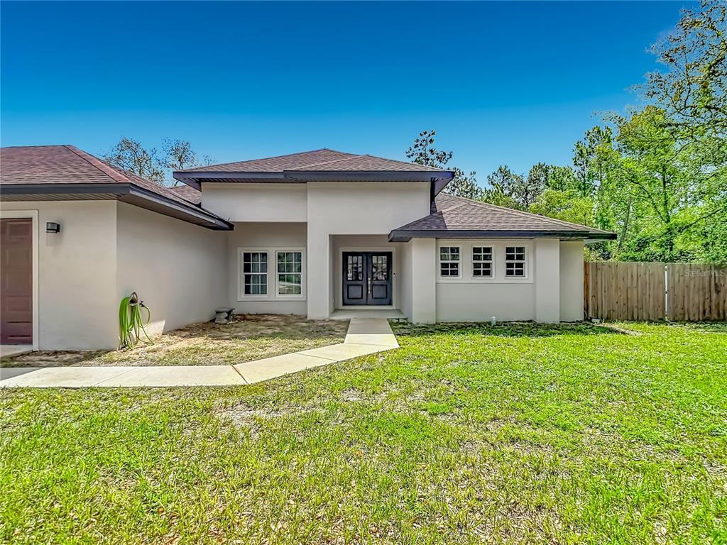 A single-story house with a light-colored exterior, a dark roof, and a concrete walkway — 15032 HUMMINGBIRD ROAD, WEEKI WACHEE, FL