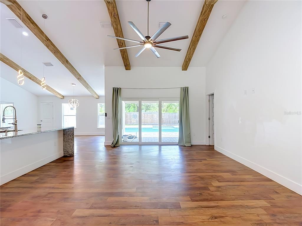 An open-concept living area features wood-look flooring, vaulted ceilings with exposed beams, and a sliding glass door — 15032 HUMMINGBIRD ROAD, WEEKI WACHEE, FL
