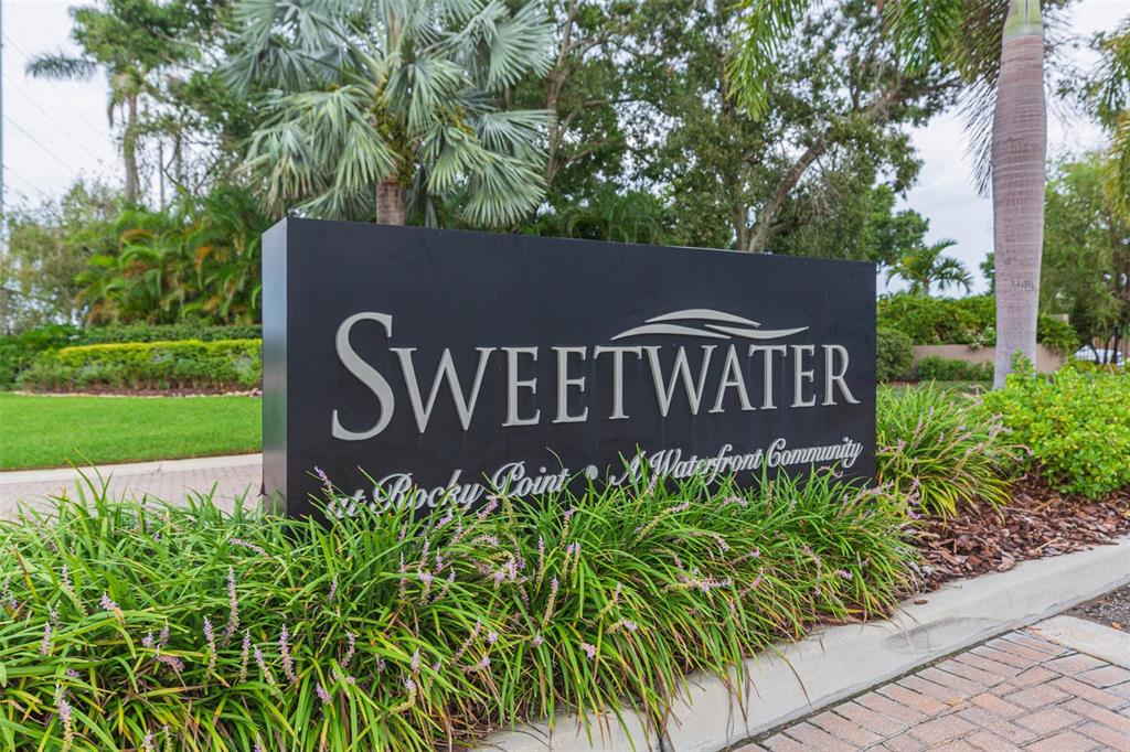 A black monument sign for Sweetwater at Rocky Point sits in a landscaped garden area — 4301 SALTWATER BOULEVARD, TAMPA, FL