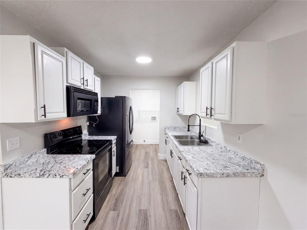 A galley kitchen features white cabinets, black appliances, and granite-look countertops — 9307 8TH AVENUE, ORLANDO, FL