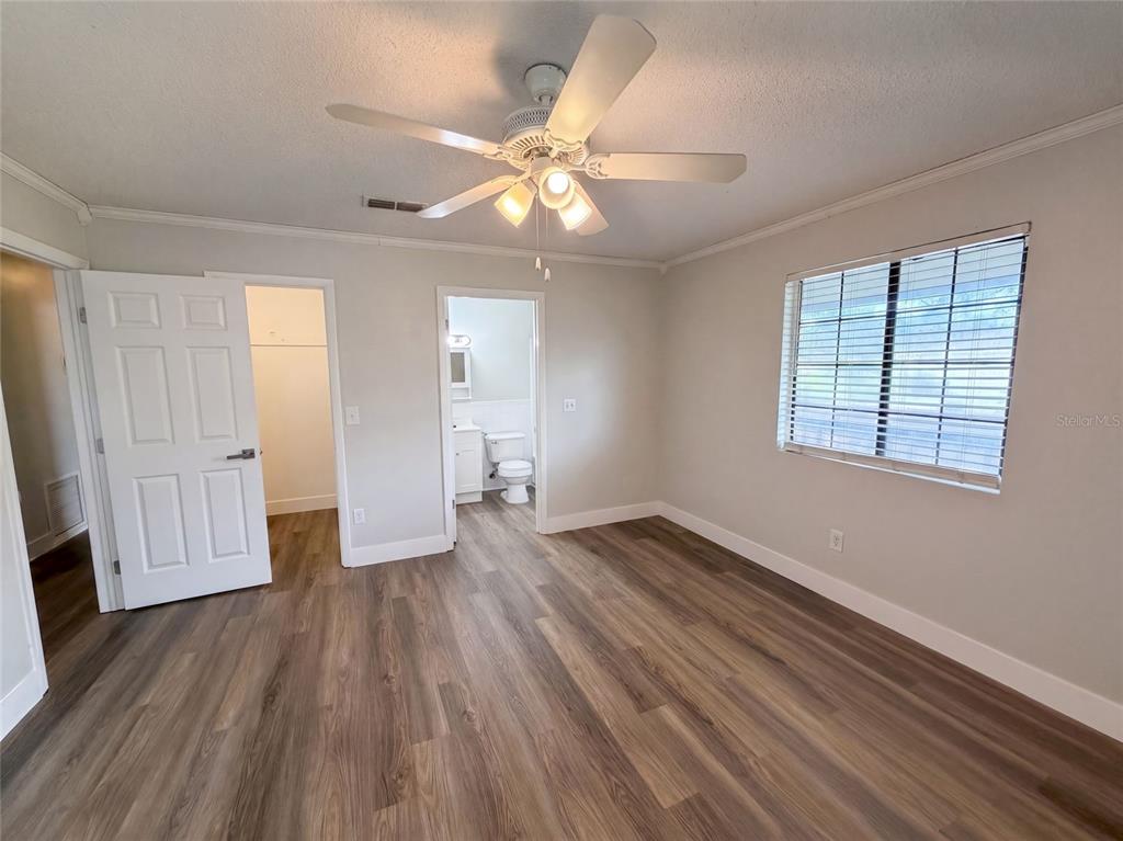 A bedroom with light gray walls, wood-look flooring, a ceiling fan, and an attached bathroom — 9307 8TH AVENUE, ORLANDO, FL