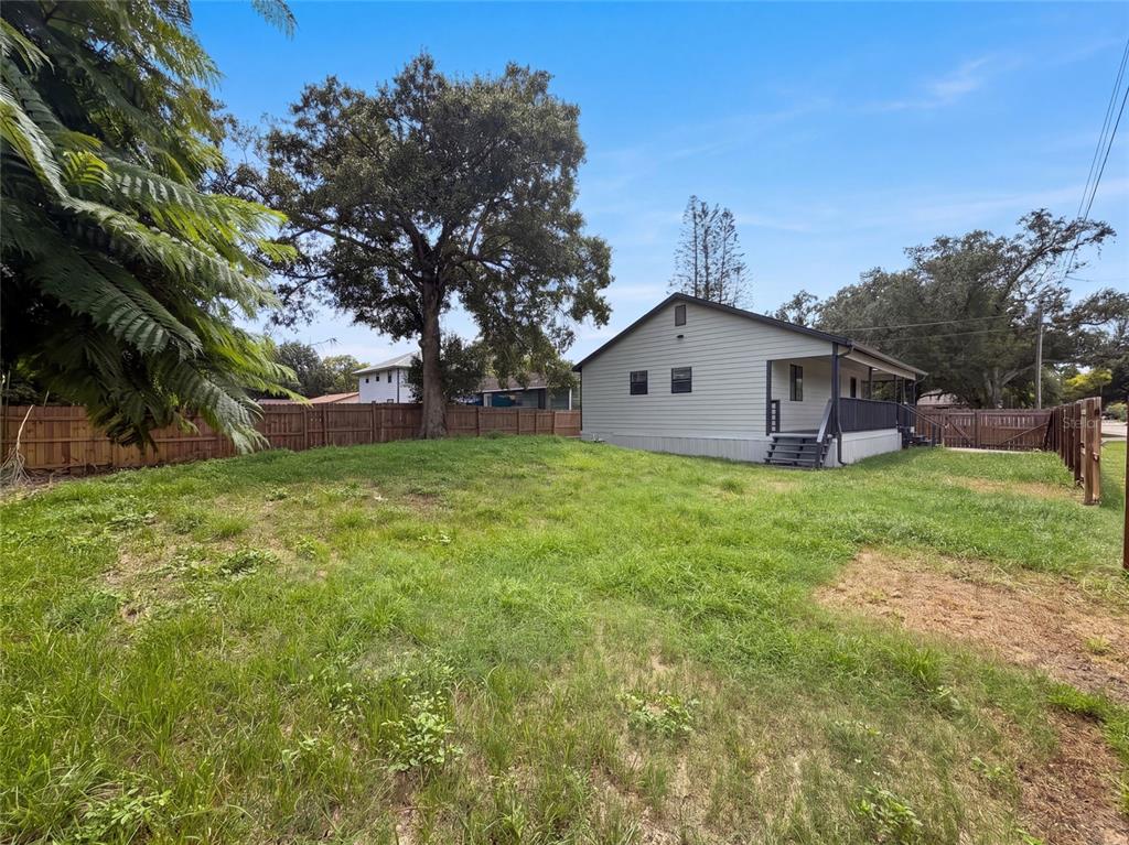 A light-colored house with a porch sits on a grassy lot enclosed by a fence — 9307 8TH AVENUE, ORLANDO, FL