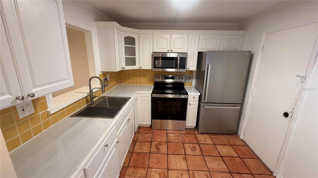 A kitchen features white cabinets, stainless steel appliances, yellow tile backsplash, and terracotta floor tiles — 406 NW 68TH AVENUE UNIT 107, PLANTATION, FL