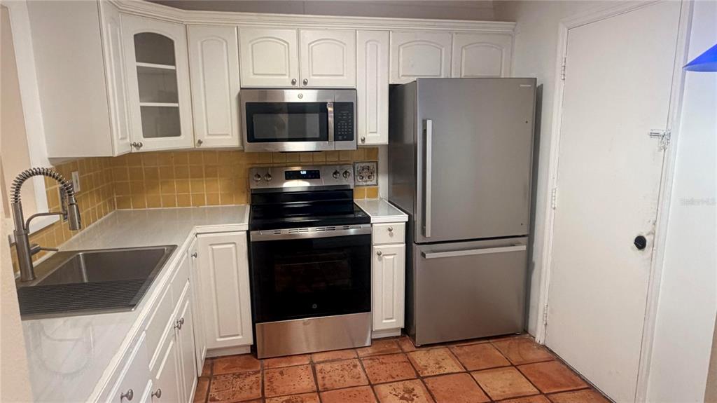 A kitchen features white cabinets, stainless steel appliances, yellow tile backsplash, and terracotta floor tiles — 406 NW 68TH AVENUE UNIT 107, PLANTATION, FL