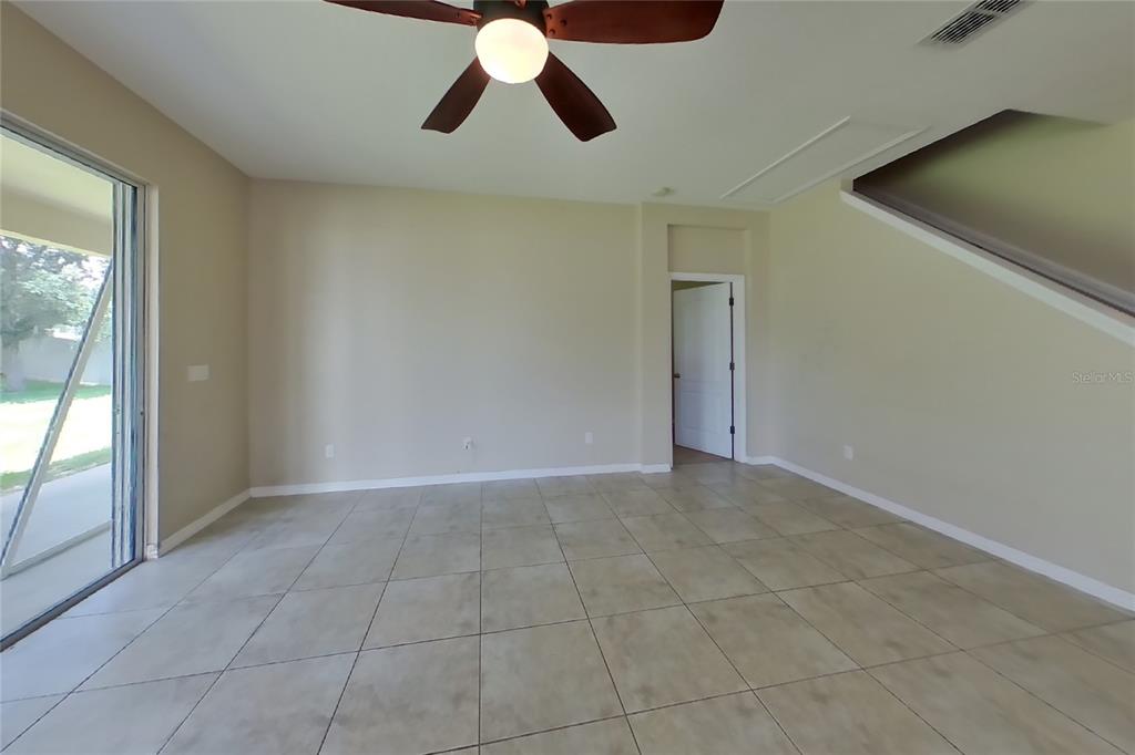 An empty room features beige tile flooring, light-colored walls, a ceiling fan, and sliding glass doors — 12552 HAMMOCK POINTE CIRCLE, CLERMONT, FL
