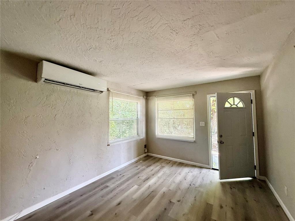 An empty room features light wood-look flooring, textured walls, two windows, and a wall-mounted air conditioner — 808 PALM BLUFF STREET UNIT D, CLEARWATER, FL