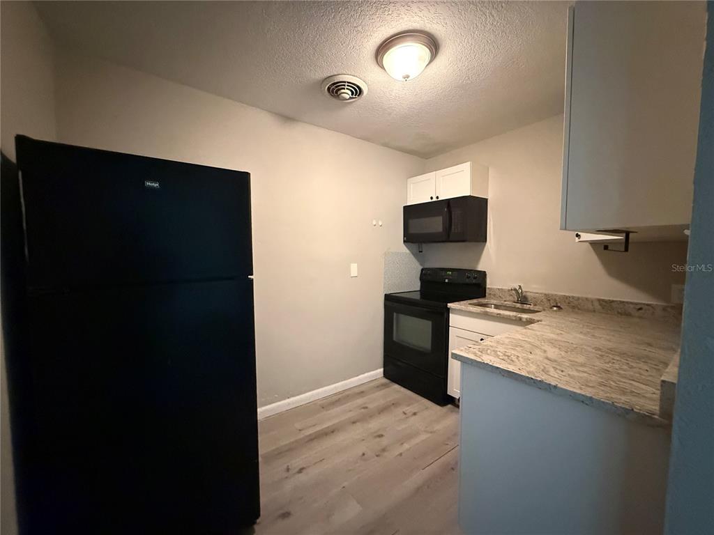 A small kitchen features black appliances, white cabinets, and light-colored stone countertops — 808 PALM BLUFF STREET UNIT D, CLEARWATER, FL