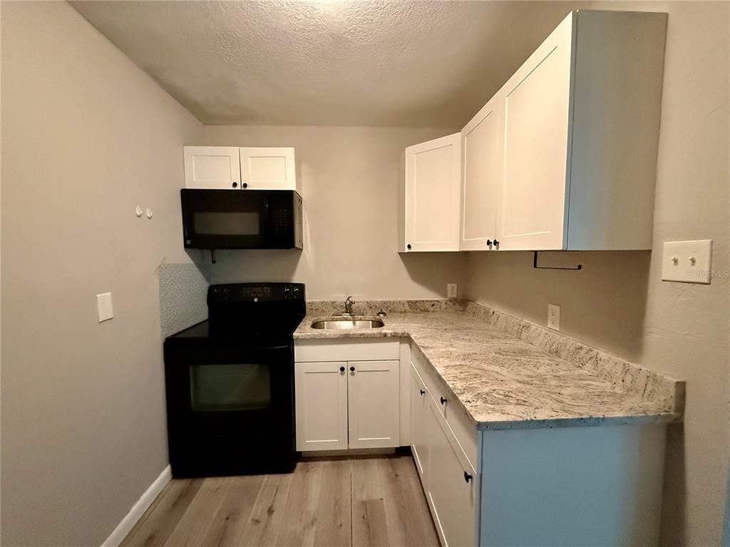 A kitchen features white cabinets, granite countertops, and black appliances against light gray walls — 808 PALM BLUFF STREET UNIT D, CLEARWATER, FL