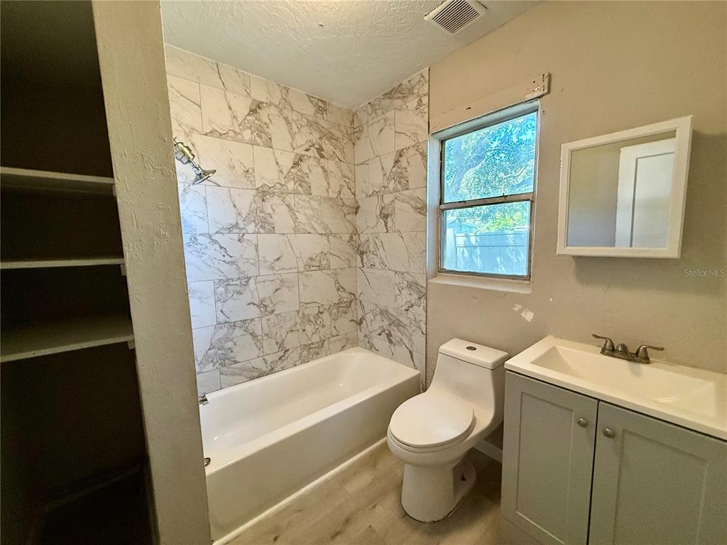 A bathroom features a marble-tiled shower-tub combo, a white toilet, and a gray vanity — 808 PALM BLUFF STREET UNIT D, CLEARWATER, FL