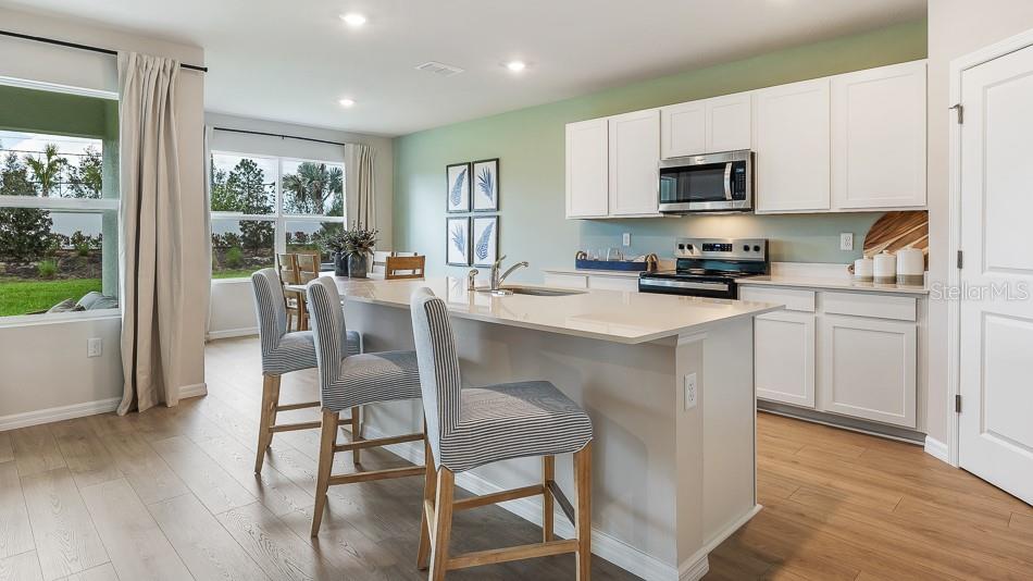 A kitchen features white cabinets, a quartz island with bar seating, and light wood flooring — 13147 BENDING CREEK TRAIL, PARRISH, FL