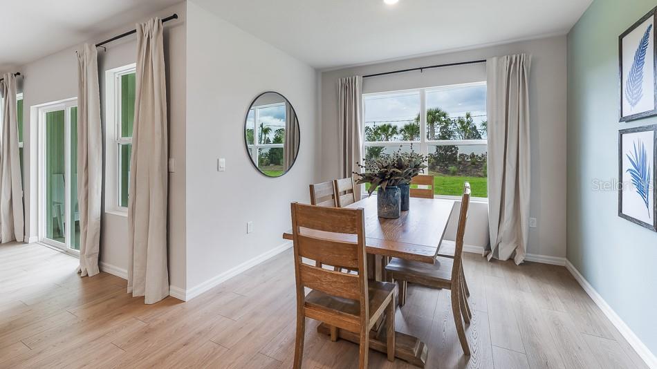 A dining room features a wooden table, chairs, light wood flooring, and large windows — 13147 BENDING CREEK TRAIL, PARRISH, FL