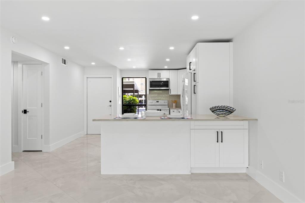 A modern kitchen features white cabinets, stainless steel appliances, and light-colored tile flooring — 2614 COVE CAY DRIVE UNIT 106, CLEARWATER, FL