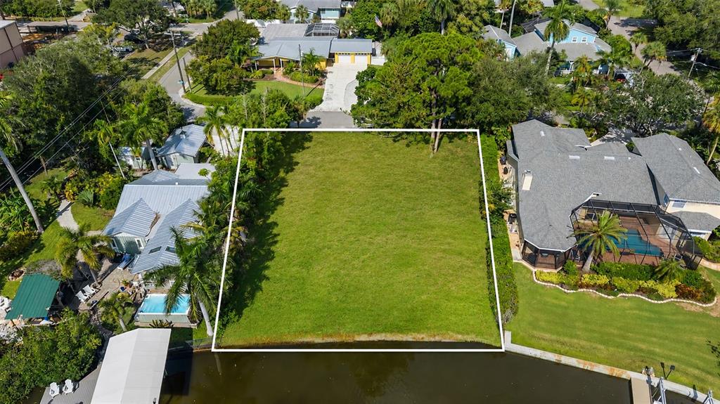 An aerial view shows a vacant, rectangular waterfront lot situated between two residential homes — 103 40TH STREET COURT NW, BRADENTON, FL