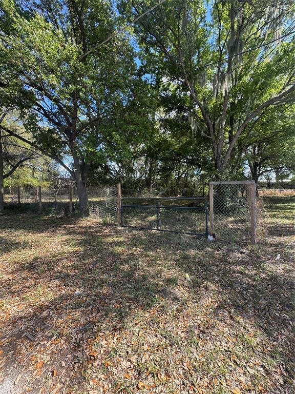 A metal gate stands in a chain-link fence surrounded by large, leafy trees — 0 DENMARK STREET, BARTOW, FL