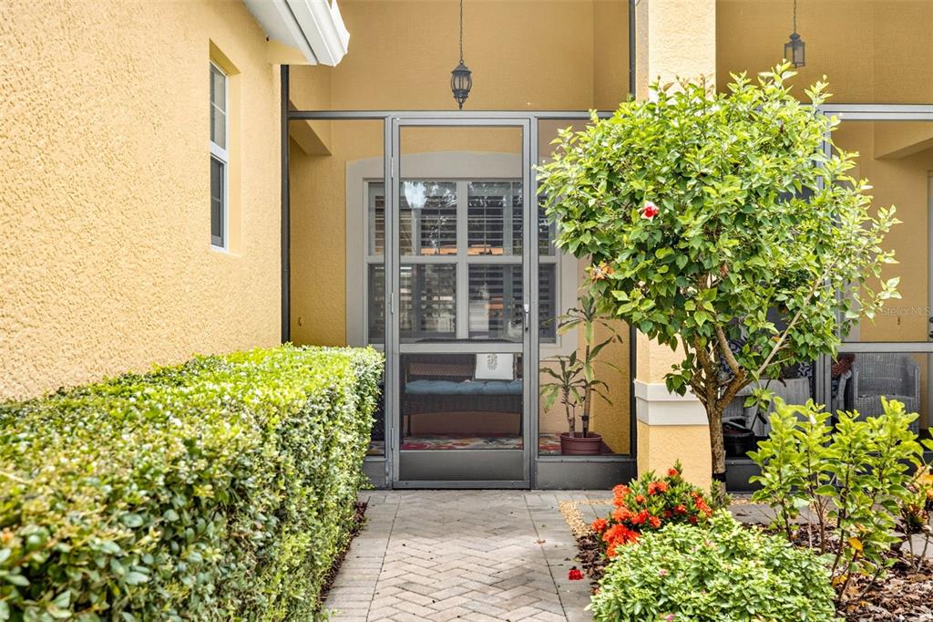 A paved walkway leads to a screened-in porch entrance with a hedge and landscaping — 16227 AMETHYST KEY DRIVE, WIMAUMA, FL