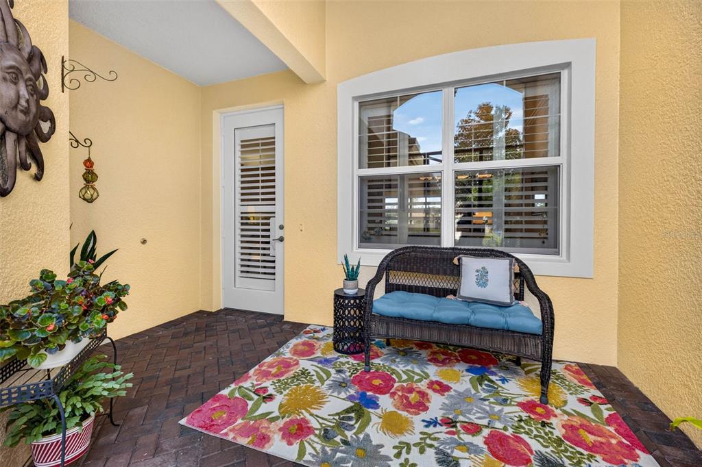 A covered patio features a brick floor, a floral rug, a wicker bench, and a window — 16227 AMETHYST KEY DRIVE, WIMAUMA, FL