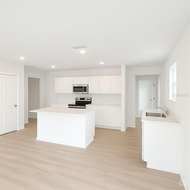 A modern kitchen features white cabinetry, a central island, and light wood-look flooring — 12915 RED DEER PLACE, PARRISH, FL