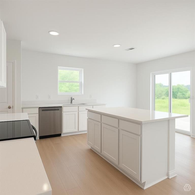 A modern kitchen features white cabinets, a central island, stainless steel appliances, and light flooring — 12915 RED DEER PLACE, PARRISH, FL
