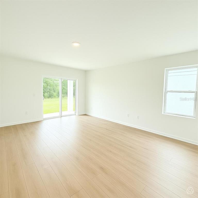 An empty room features light wood-look flooring, white walls, a sliding glass door, and windows — 12915 RED DEER PLACE, PARRISH, FL