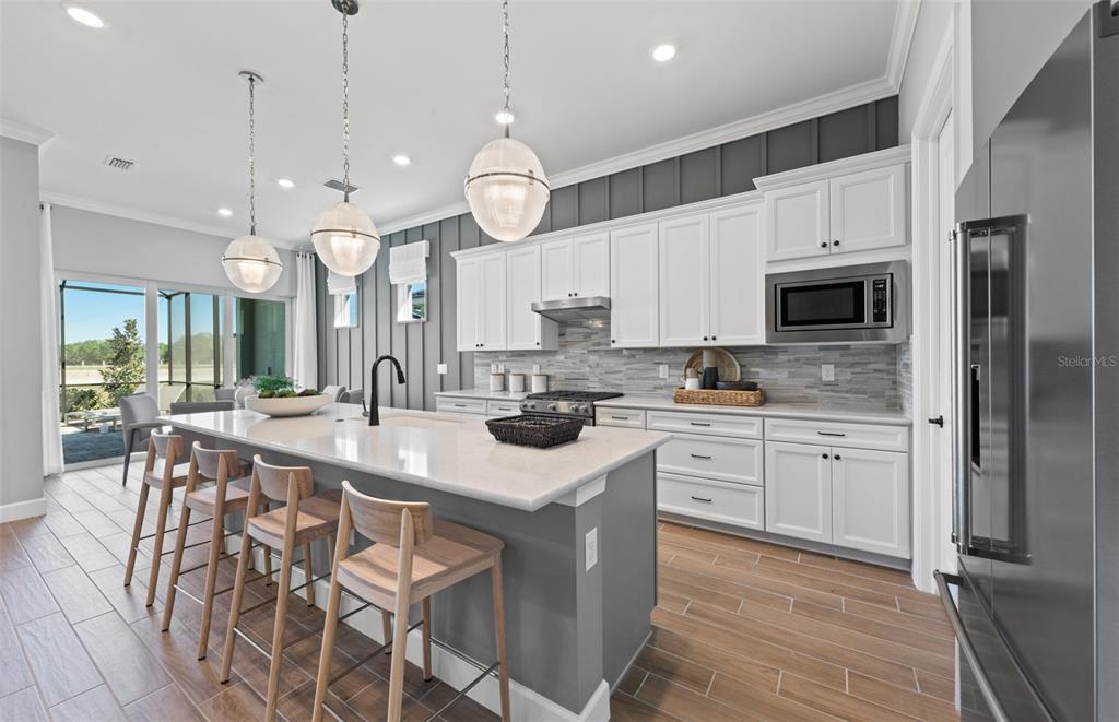 A modern kitchen features white cabinets, a gray island with bar stools, and wood-look flooring — 26641 BERING DRIVE, ENGLEWOOD, FL