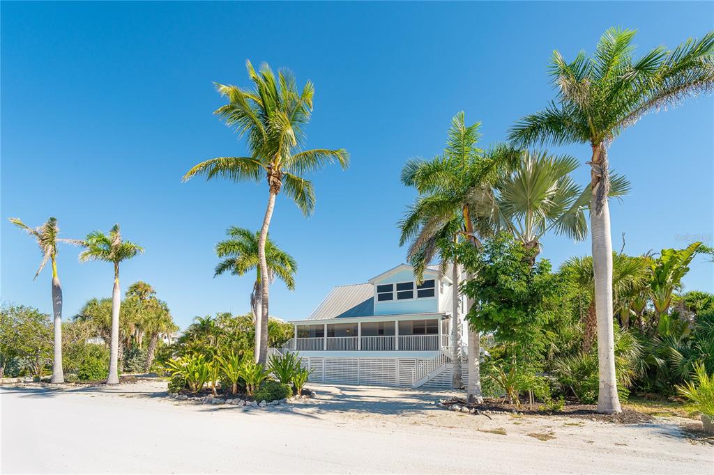 A light blue house with a screened porch stands behind palm trees on a sandy lot — 260 KETTLE HARBOR DRIVE, PLACIDA, FL