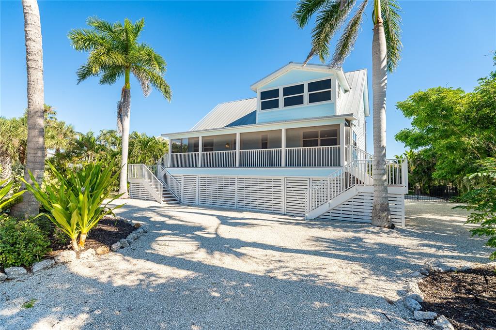 A light blue, elevated house with a screened porch and metal roof stands on gravel — 260 KETTLE HARBOR DRIVE, PLACIDA, FL