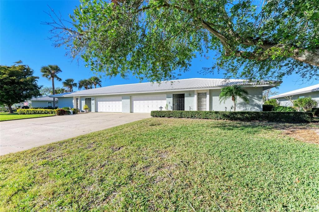A single-story duplex with white garage doors, a tiled roof, and a grassy front yard — 6704 11TH AVENUE W, BRADENTON, FL