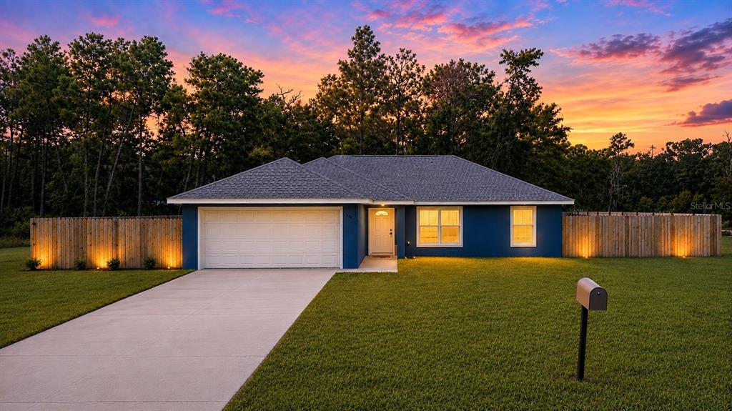 A blue single-story house with a two-car garage and a wooden fence at sunset — 138 FISHER RUN, OCKLAWAHA, FL