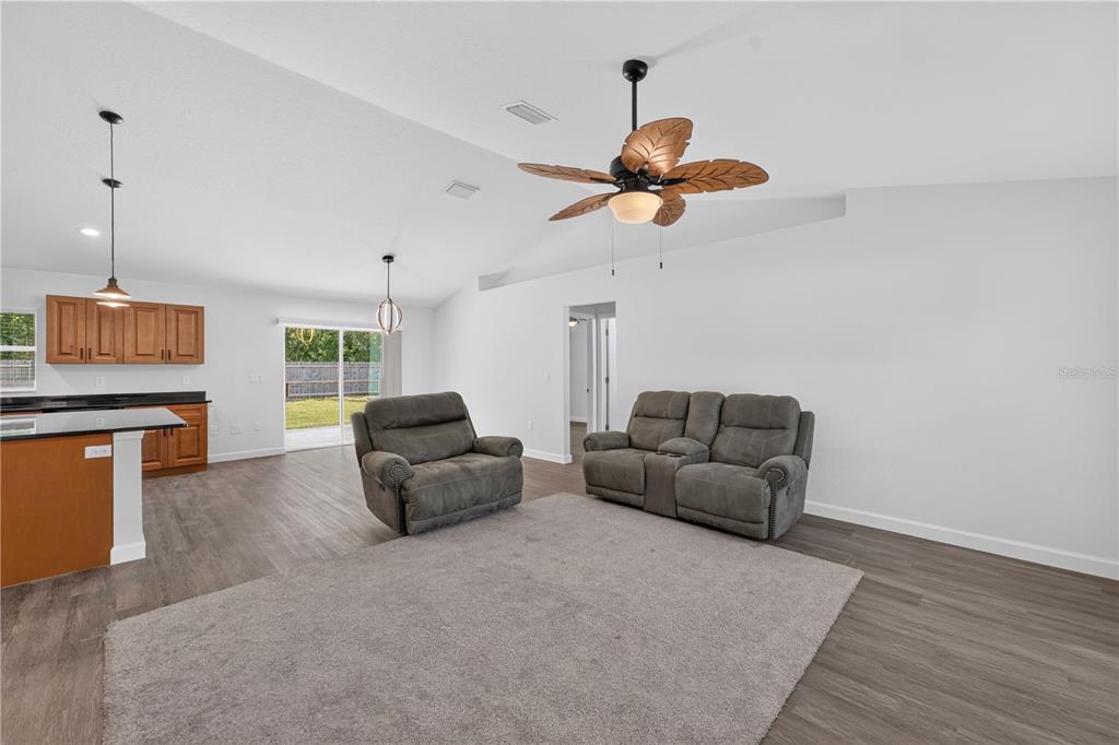 A living room with gray flooring, a gray rug, a loveseat, and a recliner — 138 FISHER RUN, OCKLAWAHA, FL