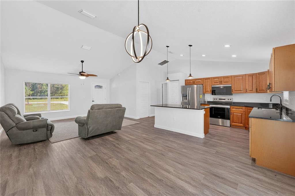An open-concept living room and kitchen with wood-look flooring, vaulted ceilings, and wooden cabinets — 138 FISHER RUN, OCKLAWAHA, FL