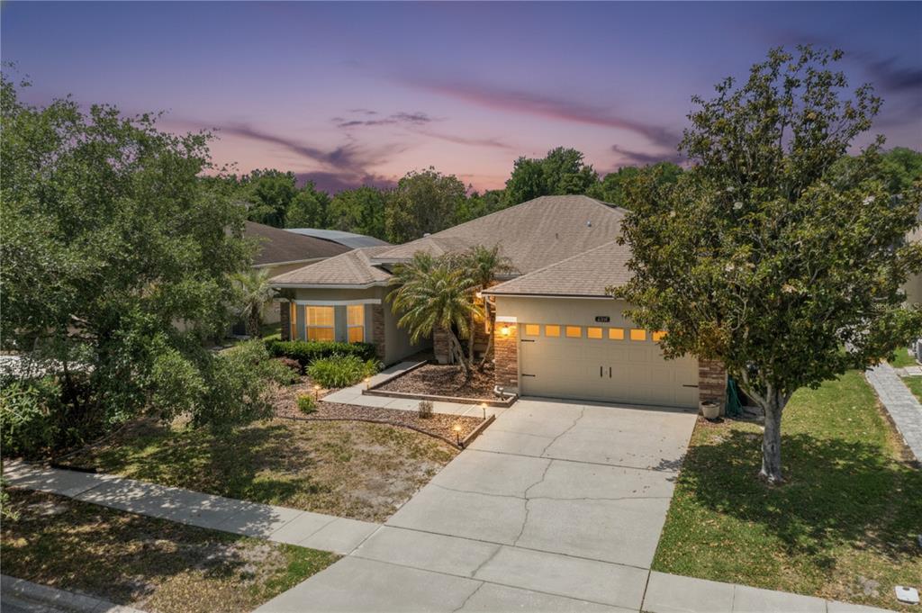 A single-story house with a green garage door, stone accents, and a large front tree — 237 STRATHMORE CIRCLE, KISSIMMEE, FL