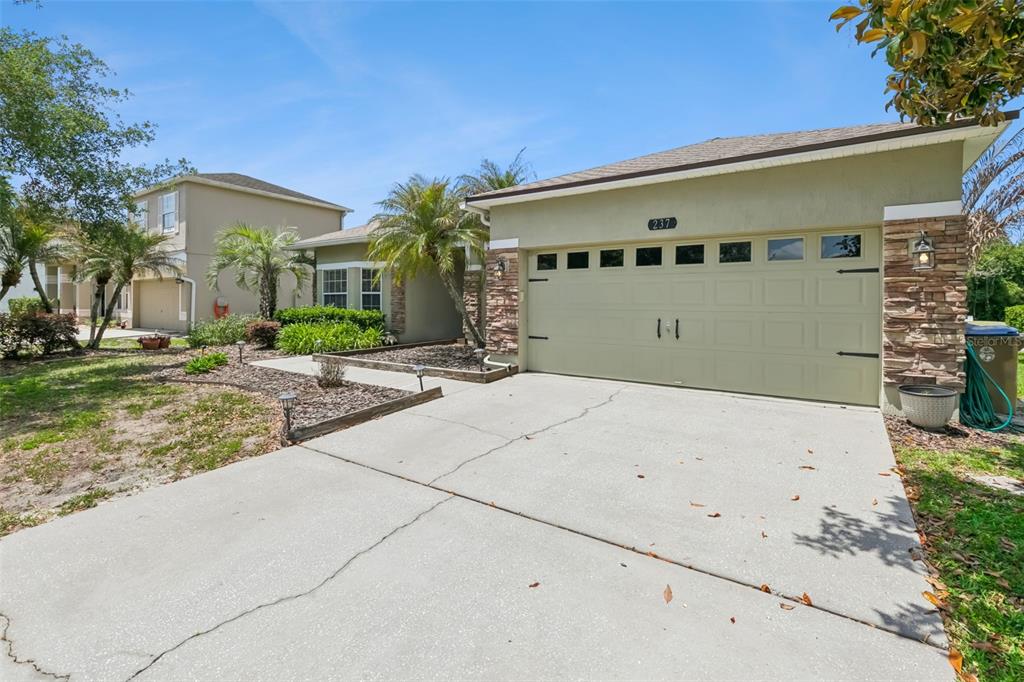 A single-story house with a tan stucco exterior, stone accents, and a palm tree garden — 237 STRATHMORE CIRCLE, KISSIMMEE, FL