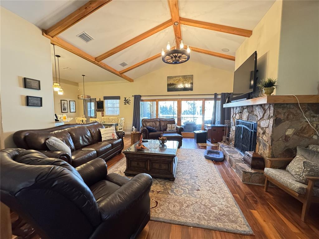 A living room features a vaulted ceiling with exposed beams, a stone fireplace, and leather furniture — 3108 N WHEATON POINT, HERNANDO, FL