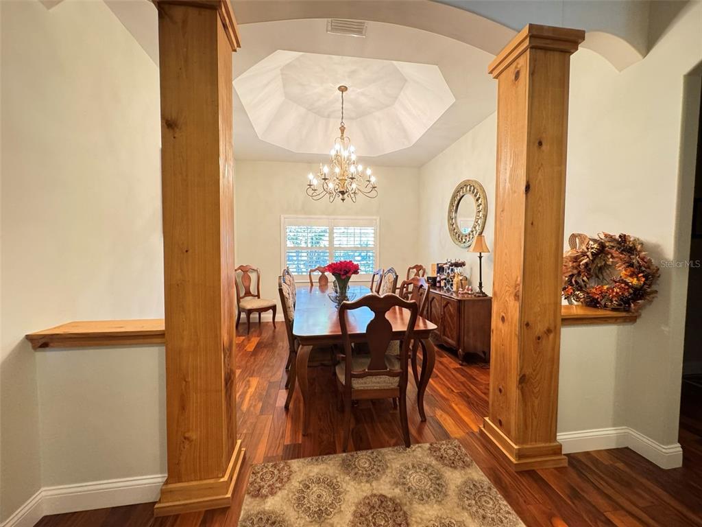 A dining room features a tray ceiling, chandelier, wooden columns, and dark hardwood flooring — 3108 N WHEATON POINT, HERNANDO, FL