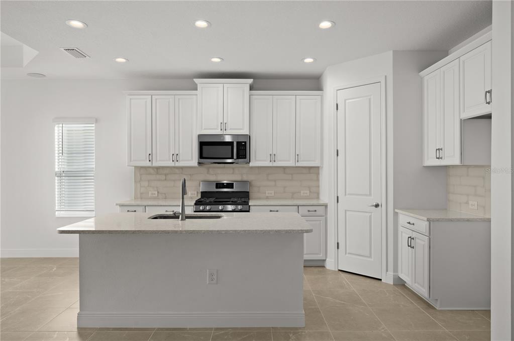 A modern kitchen features white cabinetry, a central island with a sink, and tile flooring — 10366 LAKE GEORGE AVENUE, SARASOTA, FL