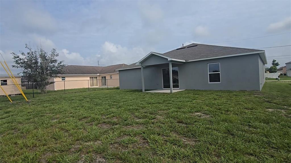 The backyard features a gray house with a covered patio and a chain-link fence — 541 LAKEVIEW COURT, POINCIANA, FL