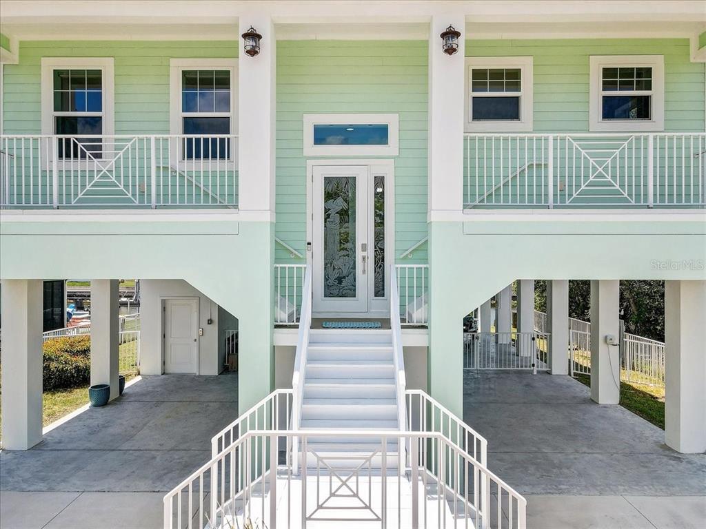 An elevated house with light green siding, white railings, and a central staircase leading upstairs — 4389 5TH ISLE DRIVE, HERNANDO BEACH, FL