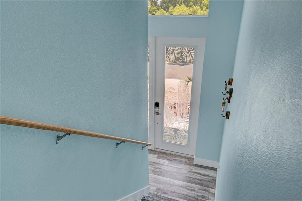 A view looking down a staircase with light blue walls toward a glass-paneled front door — 4389 5TH ISLE DRIVE, HERNANDO BEACH, FL