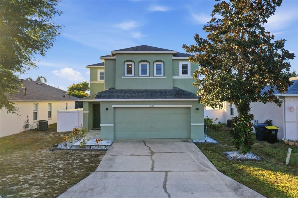 A two-story, light green stucco house features a two-car garage and a concrete driveway — 429 RONA LANE, DAVENPORT, FL
